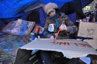 An Occupy Portland protester makes a sign under a tarp shelter.