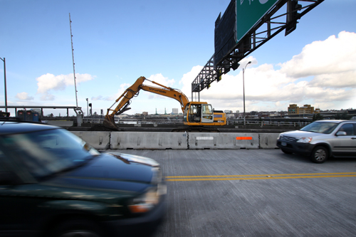 Construction equipment sits unused as cars pass by.