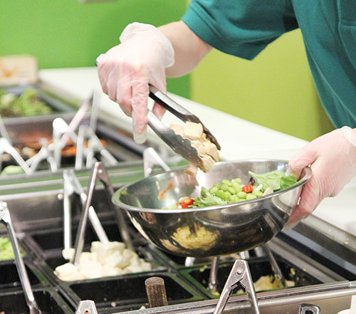 A cafeteria food service worker prepares meals for lunch. Photo by Kayla Nguyen.