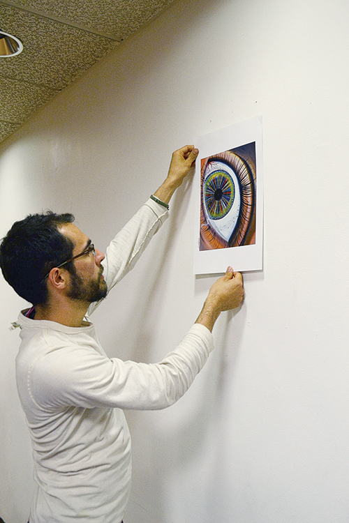 Art Show Organizer Kirk Rea hangs a student–submitted piece of art at Food For Thought Cafe on campus. Photo by Riza Liu.